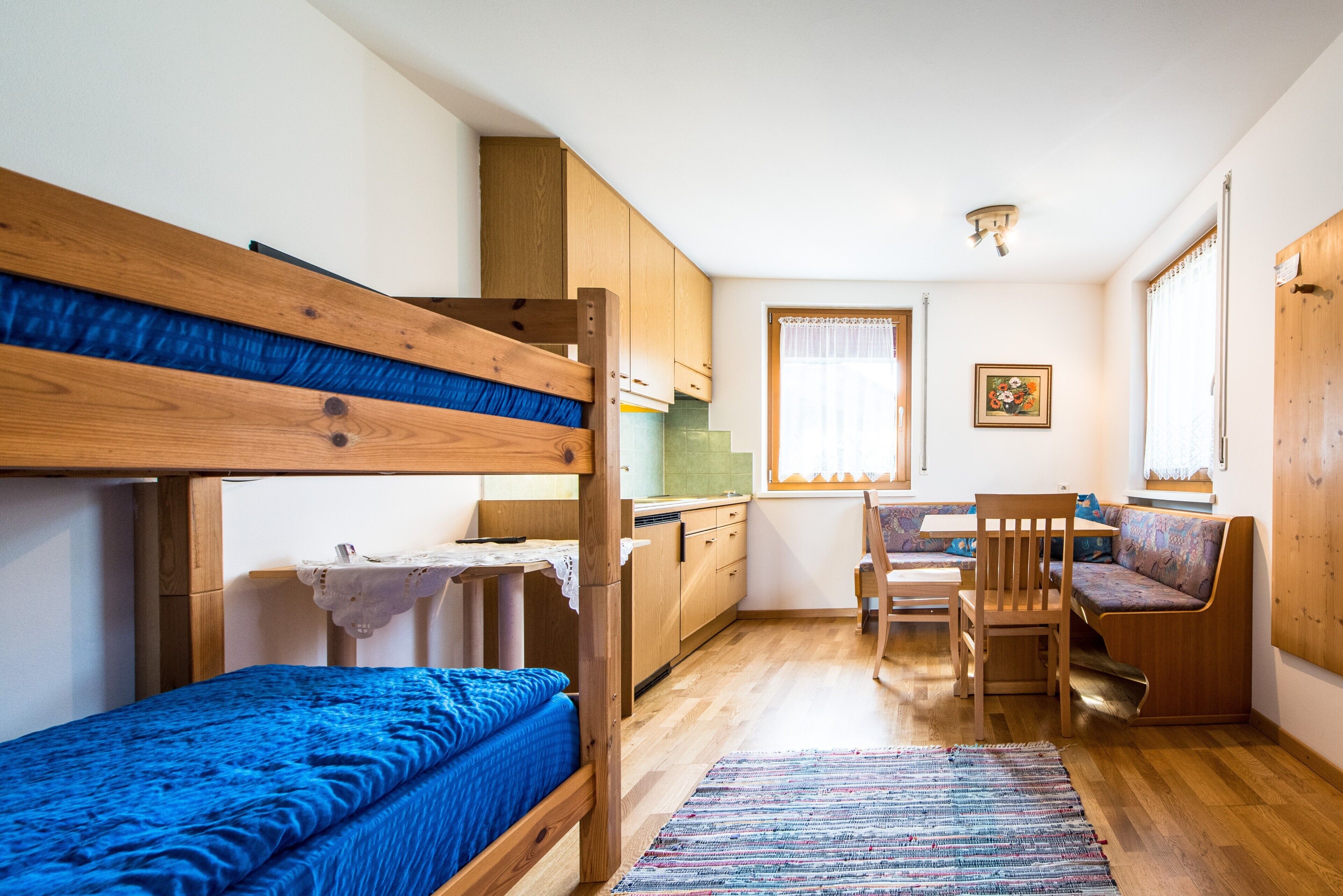 Een compacte kamer met stapelbedden, een kitchenette, een eethoek met een stoel en een raam met gordijnen.