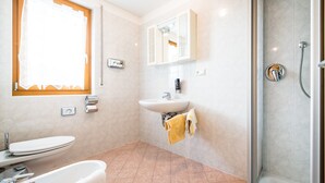 Un baño con inodoro, lavamanos, ducha y ventana con cortinas.