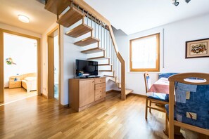 Ein Zimmer mit einer Holztreppe, einem Schreibtisch mit Computer, einem Stuhl und einem Fenster.