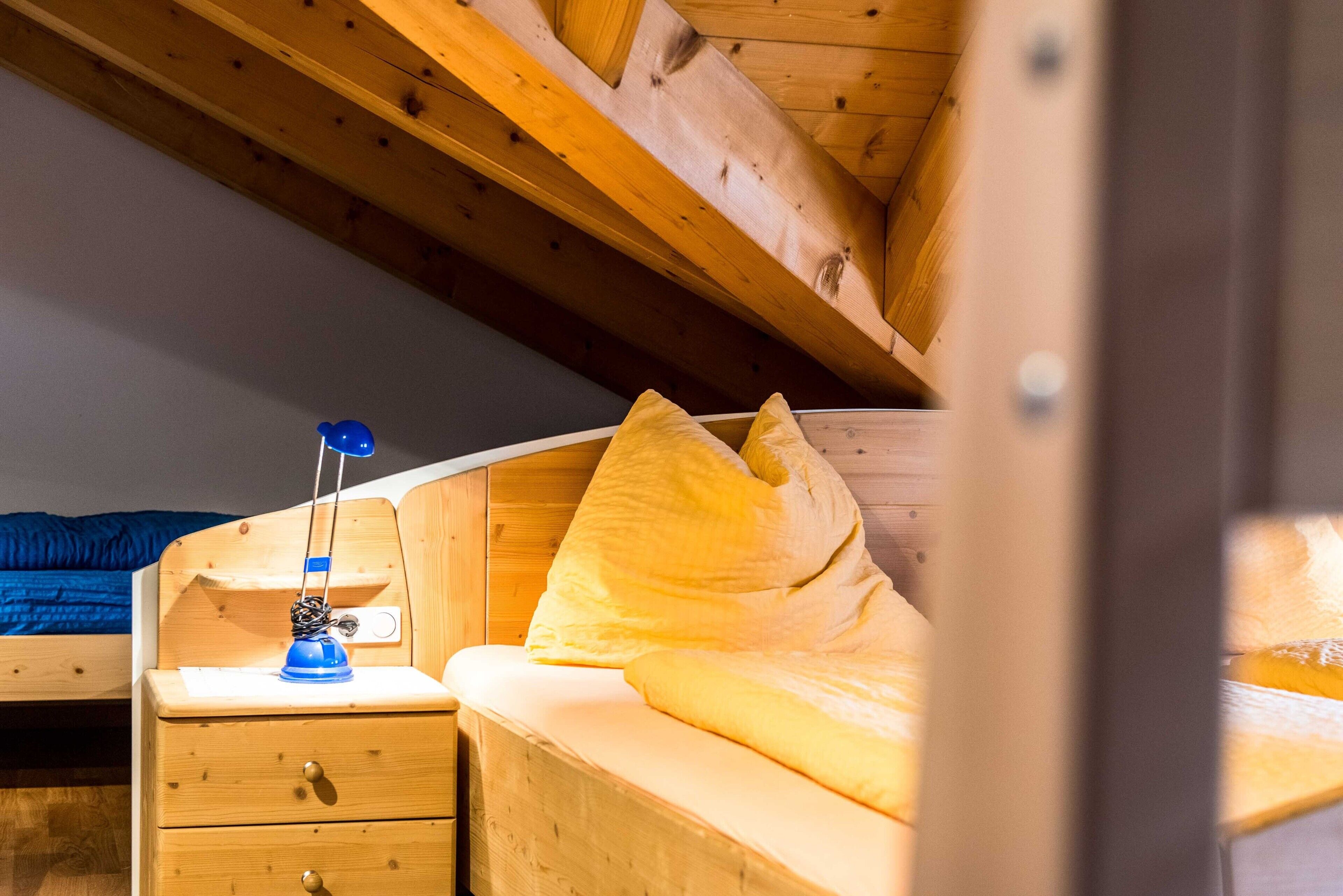 A wooden bunk bed with a nightstand, a lamp, and a pillow.