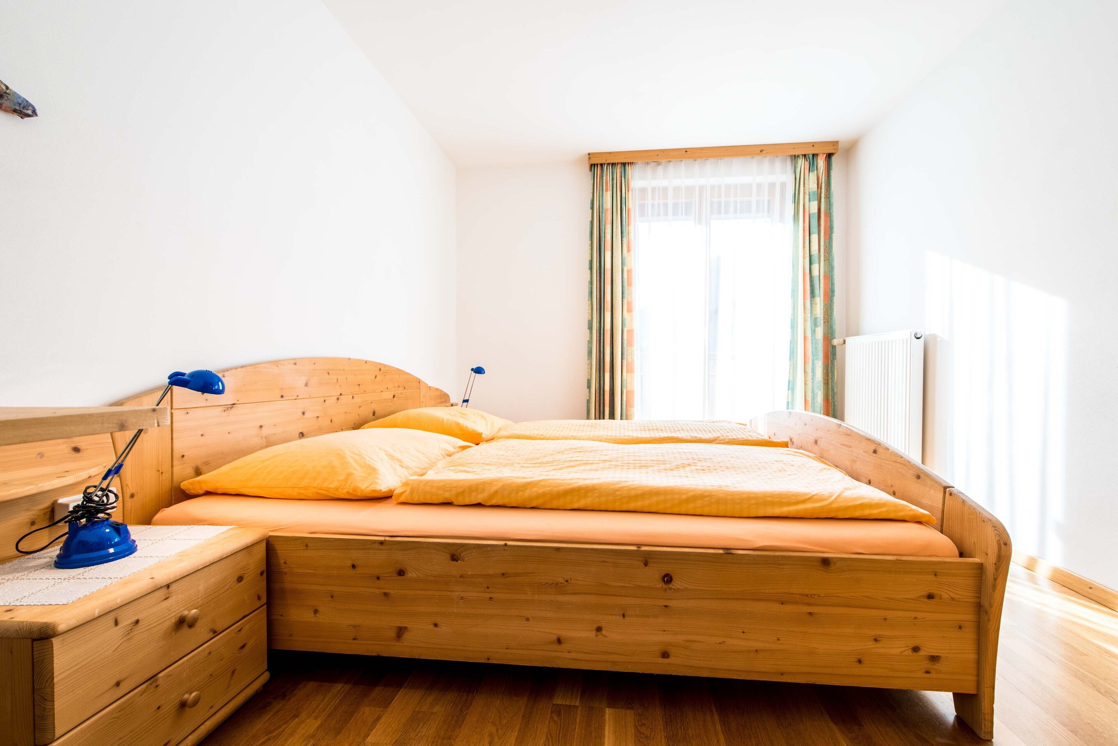 A wooden bed with a headboard, a nightstand with a lamp, and a window with curtains.