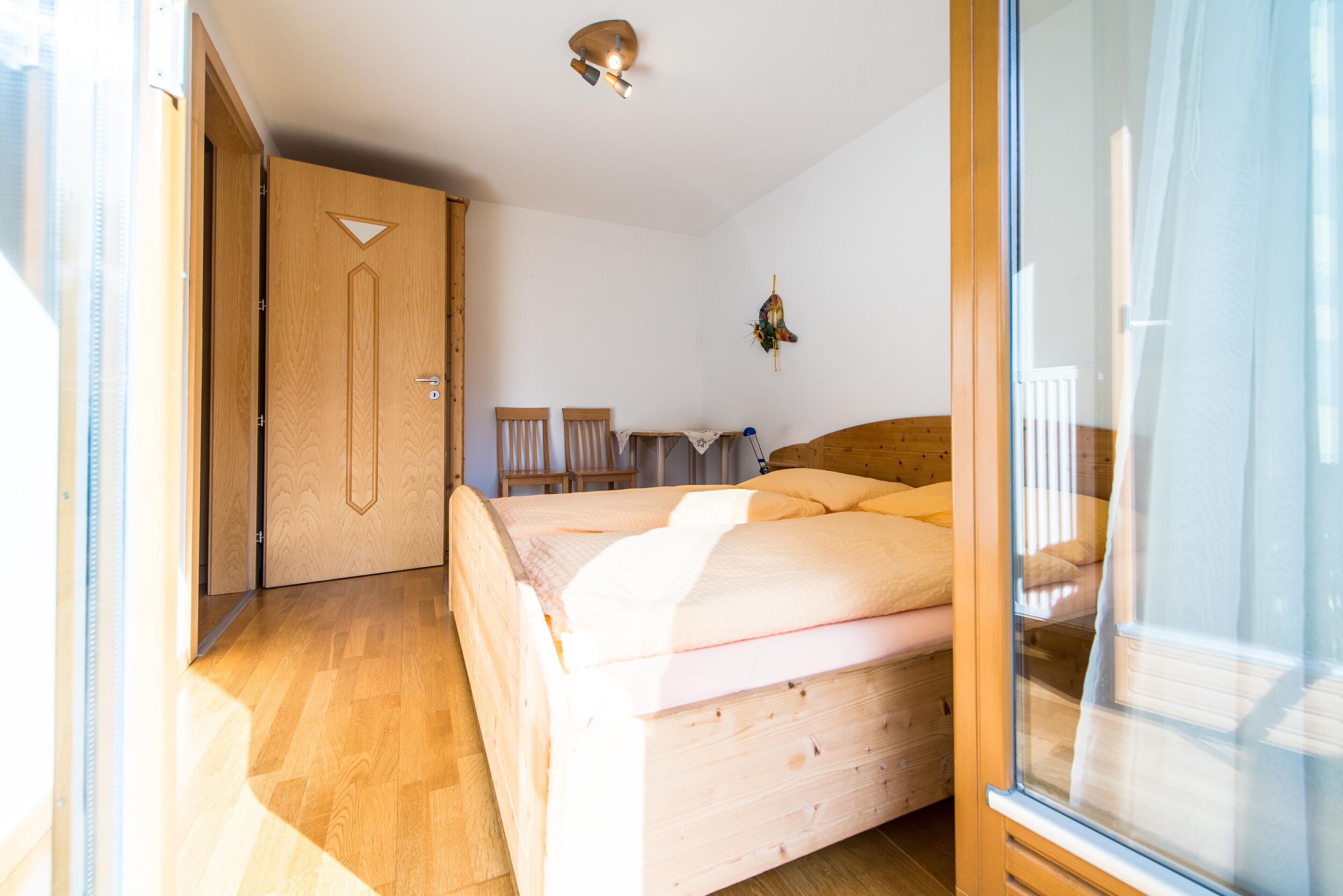 Una stanza con un letto, una porta in legno, un tavolino e una sedia.