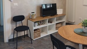Ett vardagsrum med en tv på ett tv-bord, två svarta stolar, ett runt träbord och ett vitt element.
