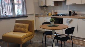 Ett kompakt bostadsutrymme med en soffa, ett matbord med stolar, en köksdel med skåp och ett fönster med gardiner.