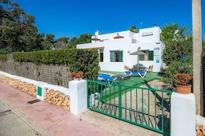 A white building with a pool, green shutters, and a green gate.