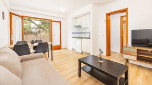 A modern living room with a sofa, dining table, and chairs, a kitchen with white cabinets, and a TV on a wooden stand.