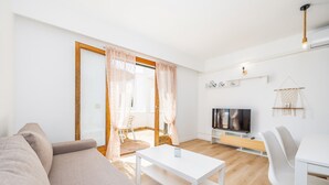 A modern living room with a sofa, a white table, a TV, and a dining area. - Apartment "Felipe 2-3" with Shared Pool, Wi-Fi & Terrace (Tourist Taxes Included) (Cala Dor)