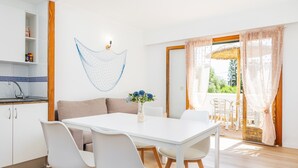 A modern kitchen with white cabinets, a sink, and a wooden countertop. There is a dining area with a white table and chairs, and a living area with a sofa and a vase of flowers. - Apartment "Felipe 2-3" with Shared Pool, Wi-Fi & Terrace (Tourist Taxes Included) (Cala Dor)