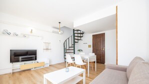 A modern living room with a flat-screen TV, white furniture, a spiral staircase, and a wooden door. - Apartment "Felipe 2-3" with Shared Pool, Wi-Fi & Terrace (Tourist Taxes Included) (Cala Dor)