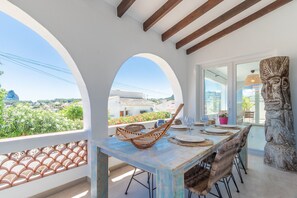 A dining area with a table set for four, a wicker chair, and a stone sculpture. - Villa "Villa Carolima - Heated Pool" with Sea View, Wi-Fi, A/C, Terrace & Garden (Benisa)