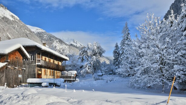 Eine Holzhütte mit einem Balkon, umgeben von schneebedeckten Bäumen und Bergen.
