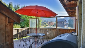 Eine Holzterrasse mit Tisch und Stühlen, einem roten Sonnenschirm und einem Grill.
