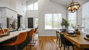 A modern kitchen with white cabinetry, a wooden dining table, and a large window with blinds.