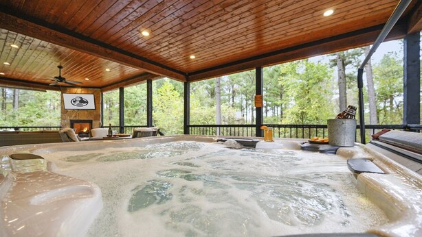 A hot tub area with a wooden ceiling and large windows overlooking a forest.