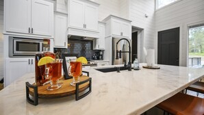 A modern kitchen with white cabinetry, a marble countertop, and a bar area with two glasses of iced tea garnished with lemon slices.