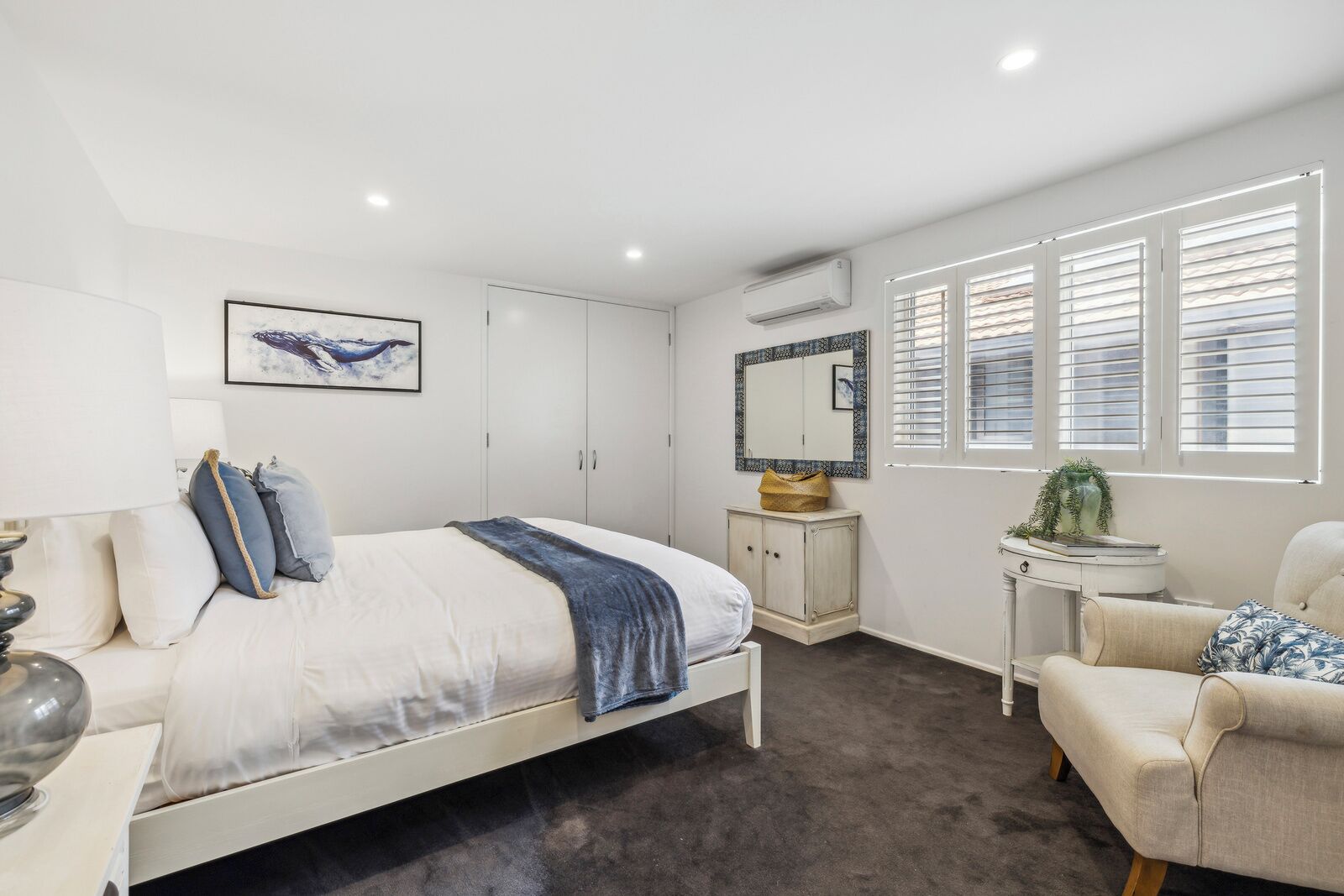 Une chambre à coucher comprenant un lit, une table de chevet, une chaise, une armoire et une fenêtre avec des stores.