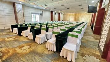 Un salón de conferencias con filas de mesas y sillas, suelo alfombrado y una pantalla grande.