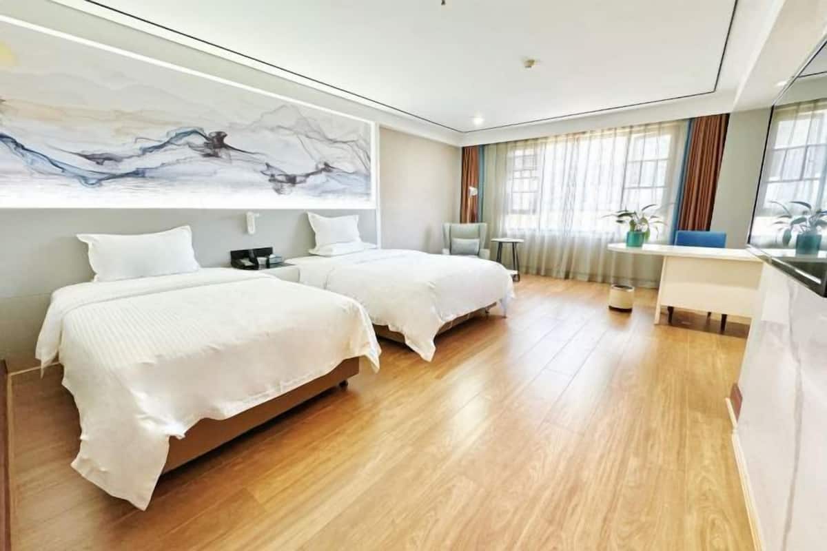 A hotel room with two beds, a desk, a chair, and a large abstract painting on the wall.