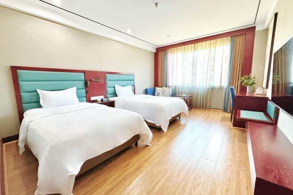 A hotel room with two beds, a desk, a chair, and a large window.