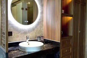 A bathroom with a round mirror, a white sink, and wooden cabinets. - Liuhe Hotel (Hengyang)