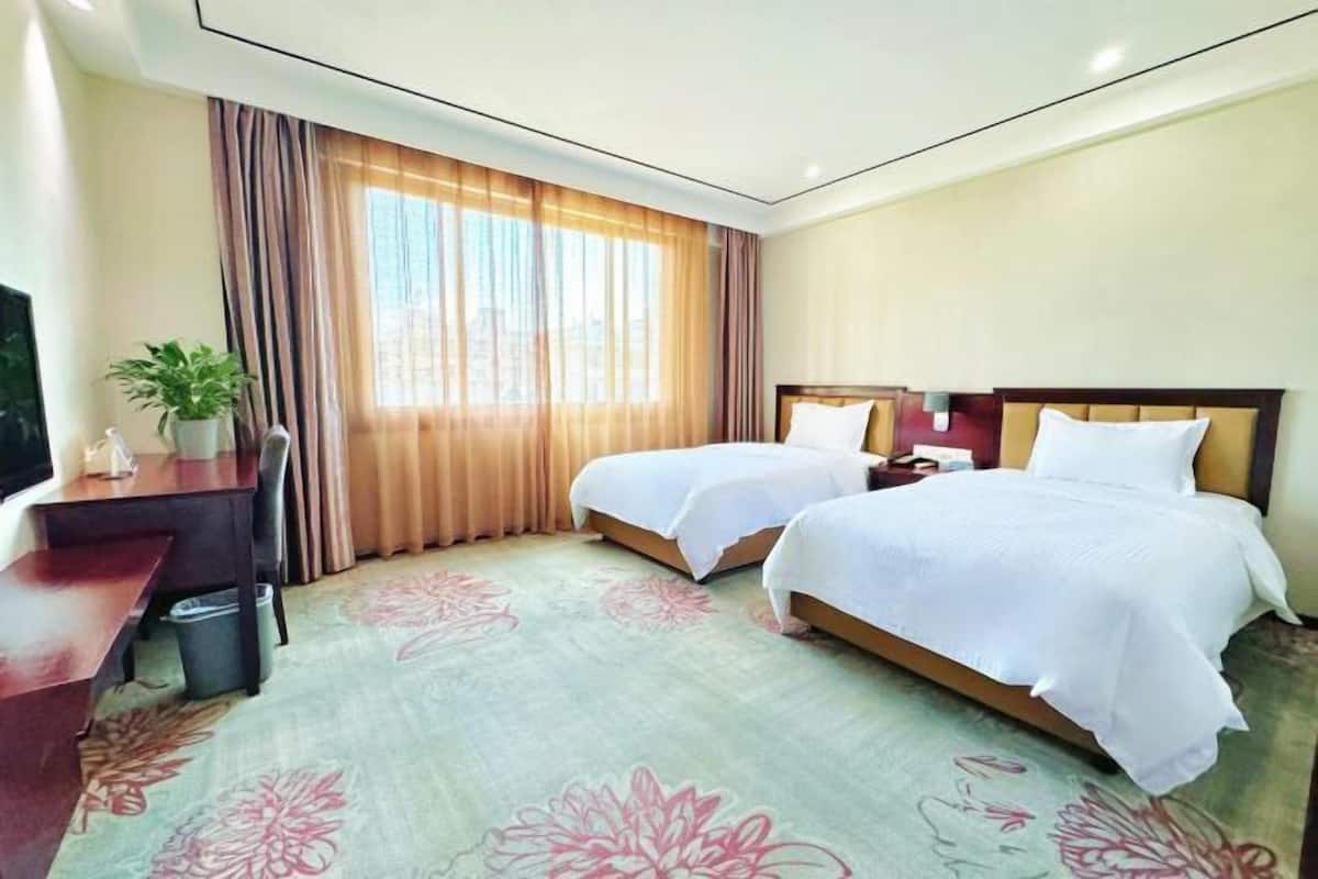 A hotel room with two beds, a desk, a TV, and a window with curtains.