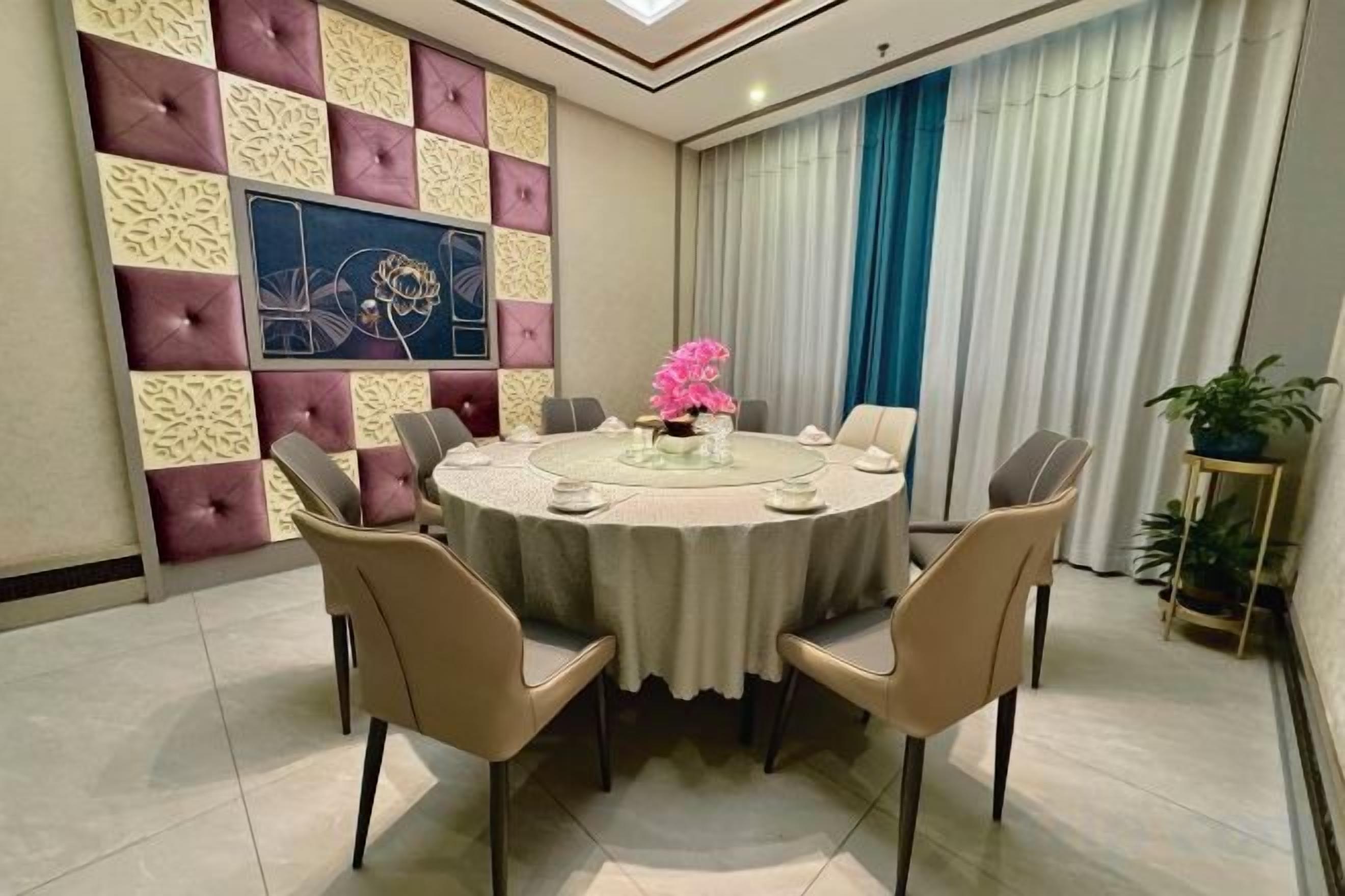 A round dining table with chairs, a vase of flowers, and a wall with a geometric pattern and a painting.