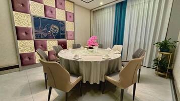 A round dining table with chairs, a vase of flowers, and a wall with a geometric pattern and a painting.