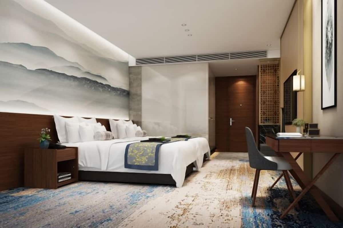 A modern hotel room with a large bed, a desk, and a wall-mounted TV.