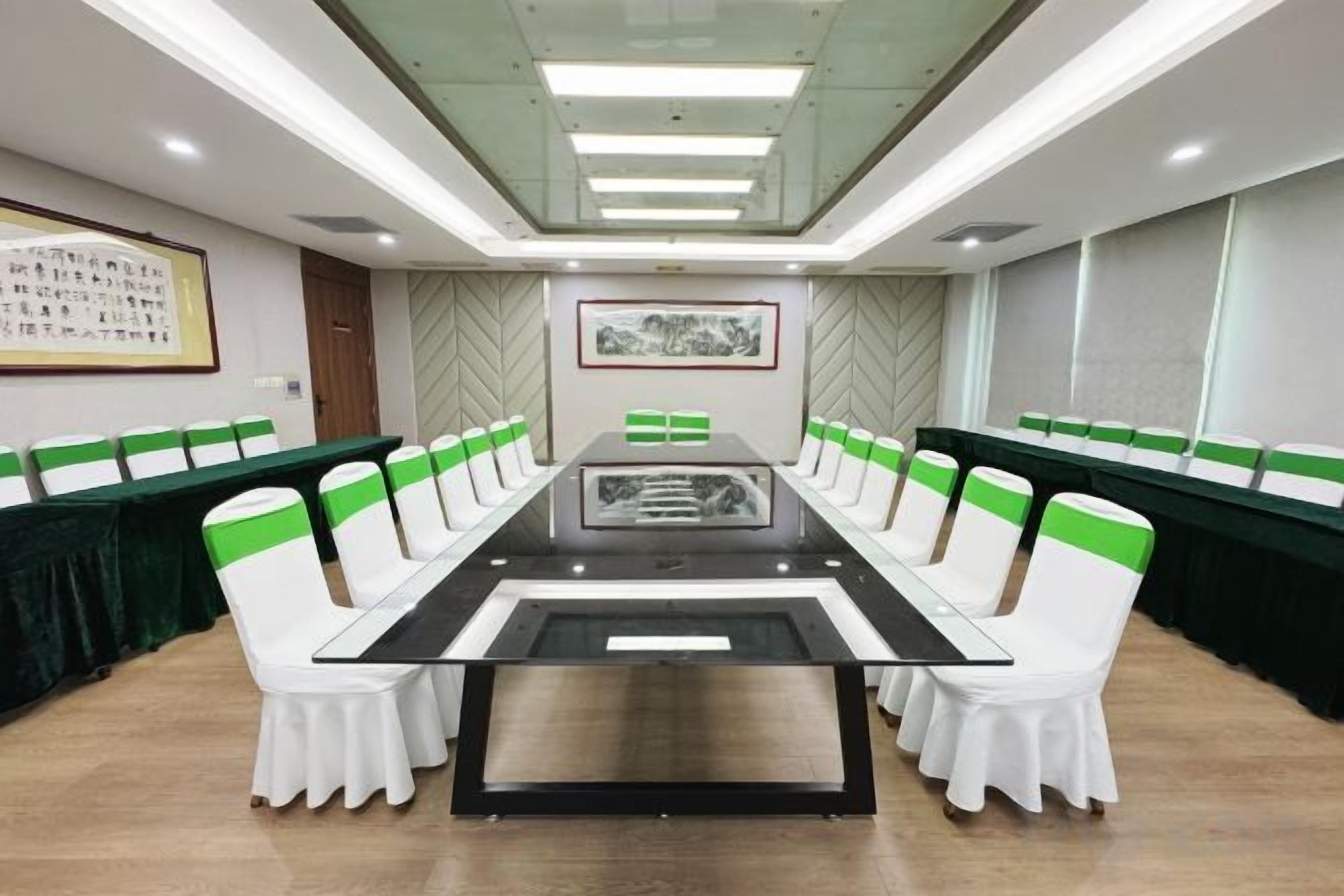 A conference room with a long table, white chairs with green sashes, and a framed picture on the wall.