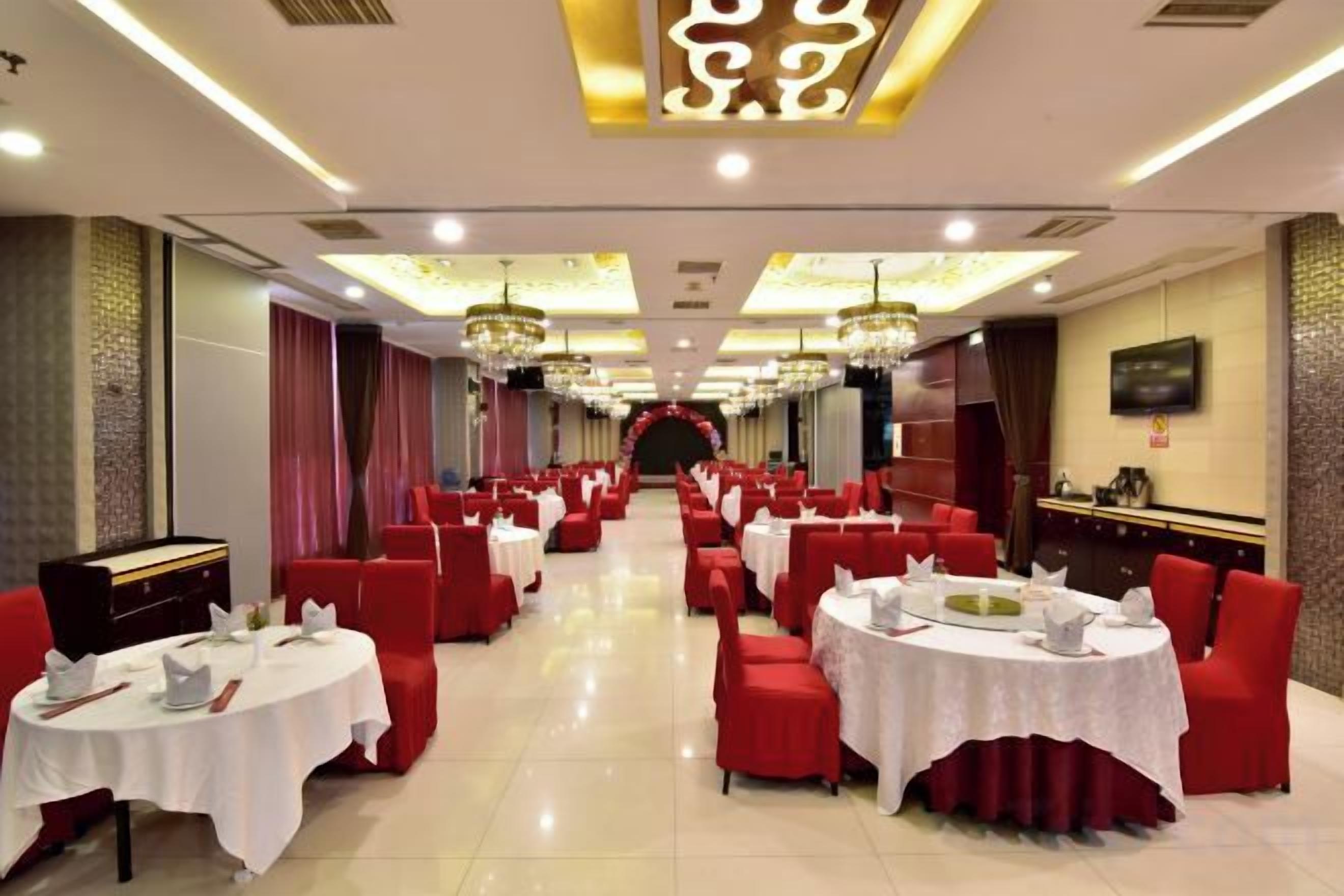 A banquet hall with round tables, red chairs, and chandeliers.