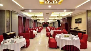 A banquet hall with round tables, red chairs, and chandeliers.