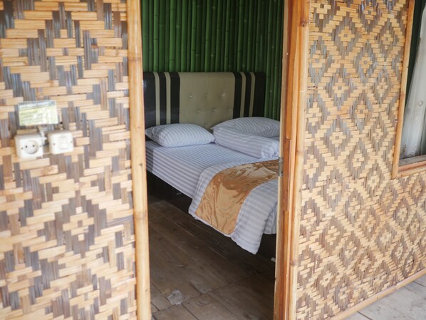 A room with a bed, a green wall, and a woven partition.