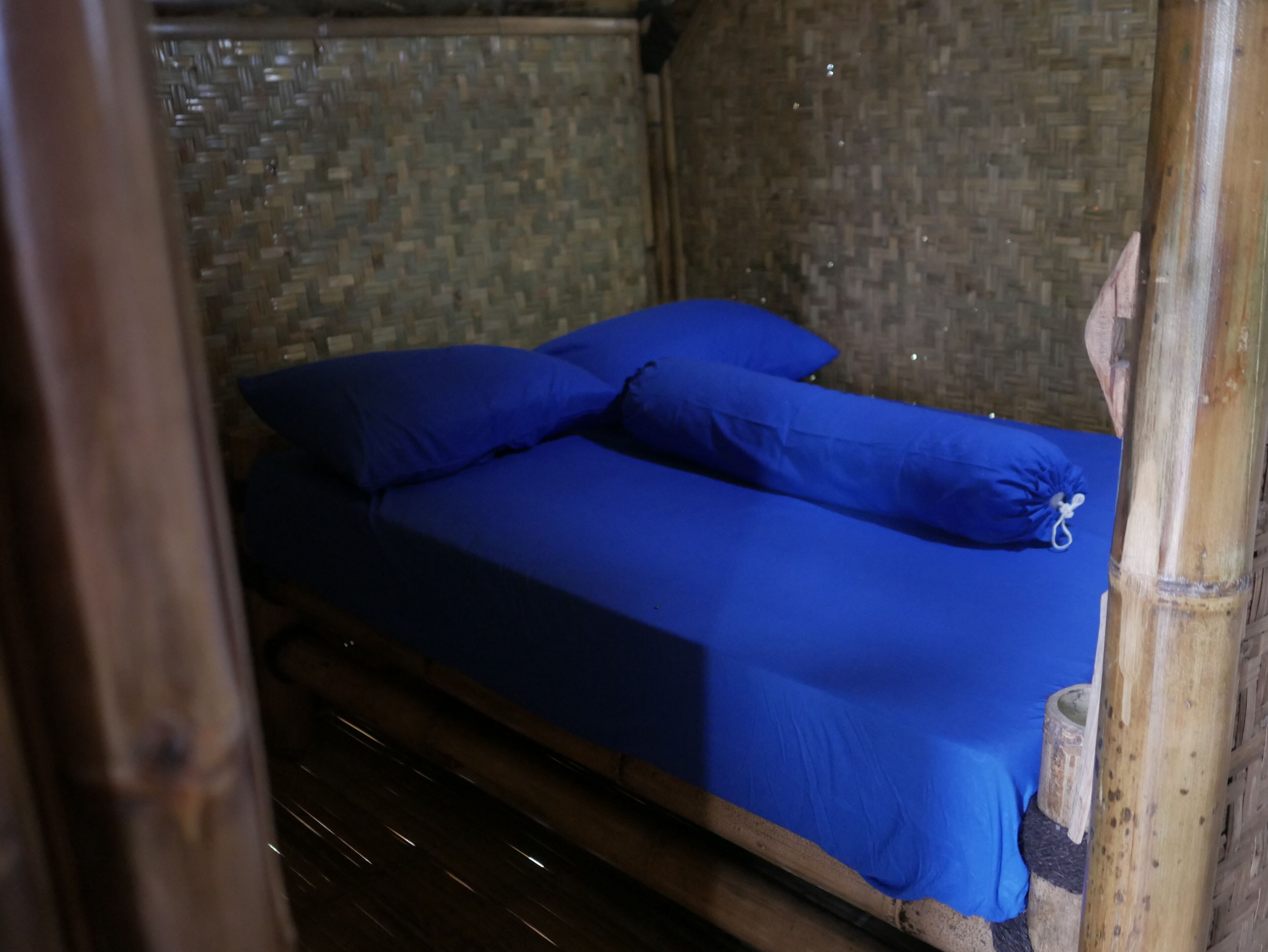A bed with blue bedding in a room with a woven wall.