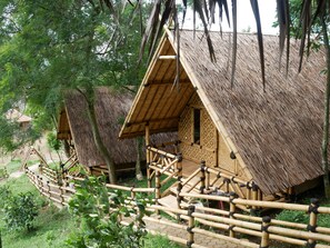 A row of thatched-roof cabins with bamboo railings, surrounded by lush greenery.