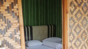 A room with a bed, green vertical blinds, and a woven bamboo wall.