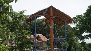 A gazebo with a thatched roof, surrounded by greenery and a paved walkway.