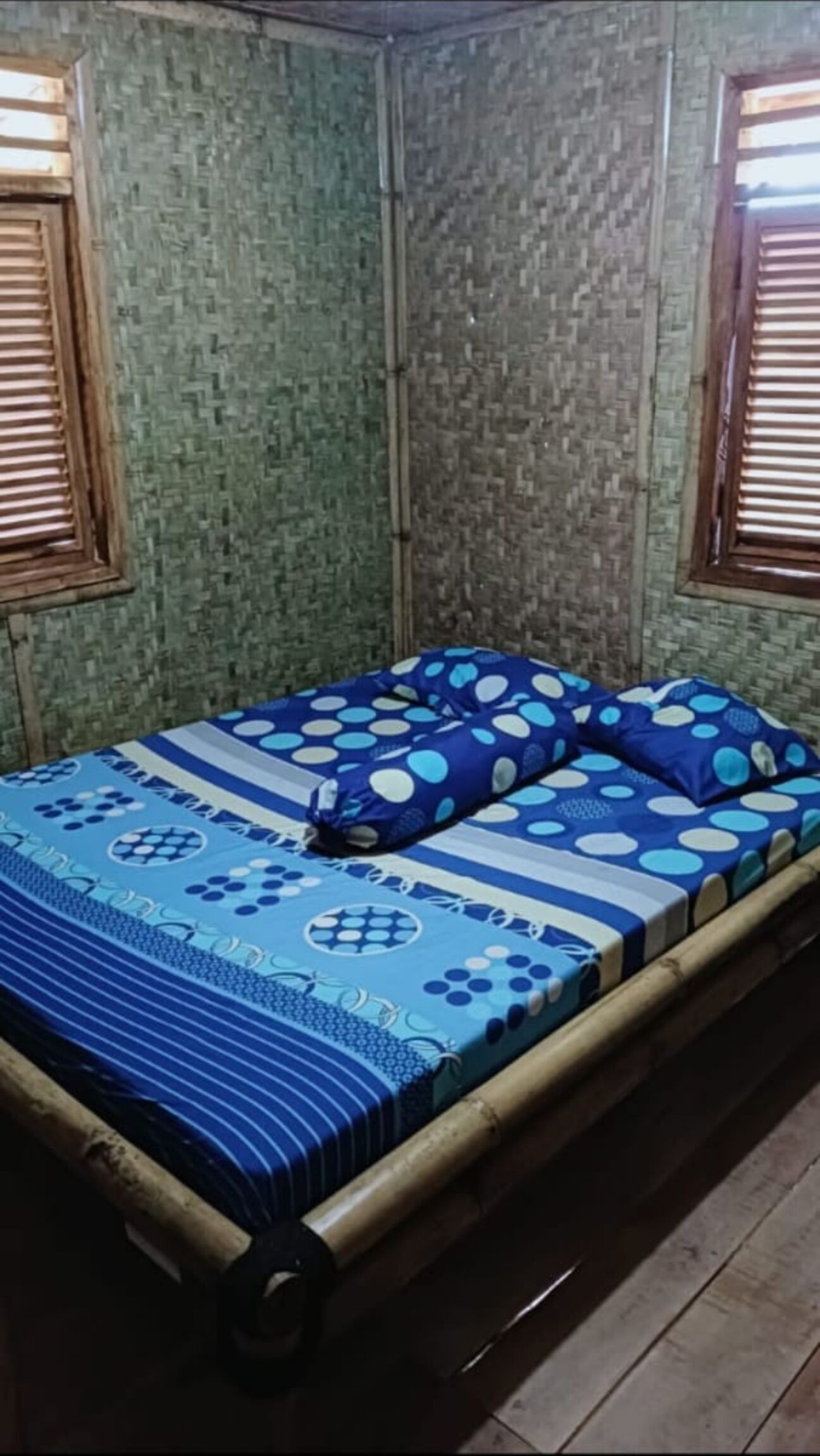 Une chambre avec un lit, deux fenêtres équipées de stores en bois et un mur orné d’un motif vert.
