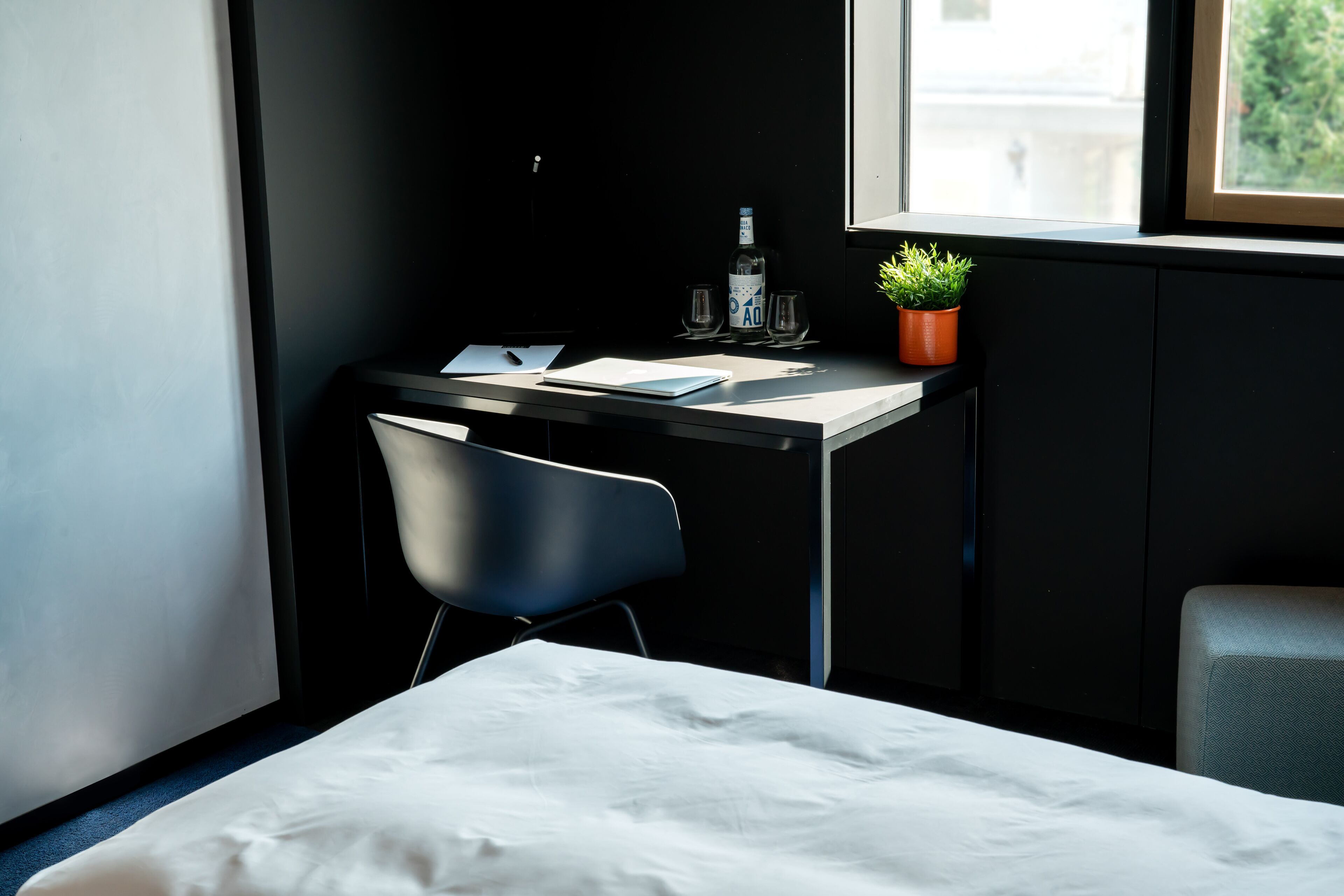 Une petite pièce moderne, équipée d’un bureau, de deux chaises, d’un lit, d’une fenêtre et d’une plante en pot.