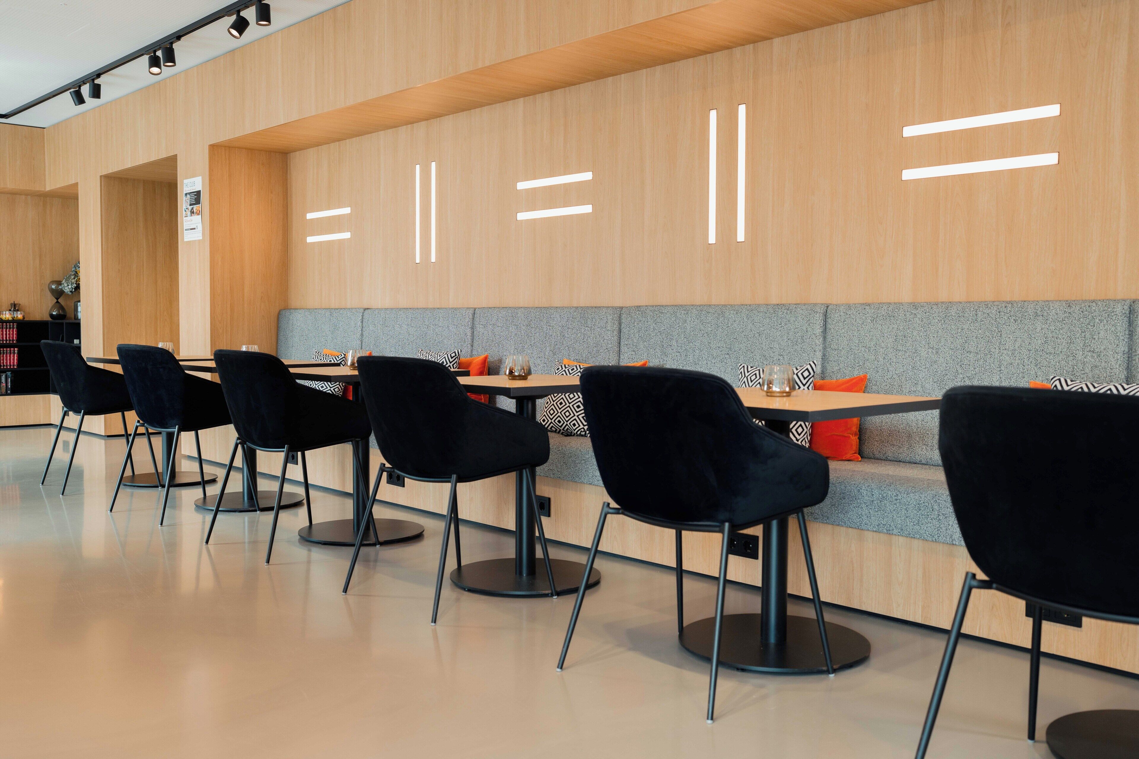 A modern dining area with black chairs, wooden tables, and a grey cushioned bench.