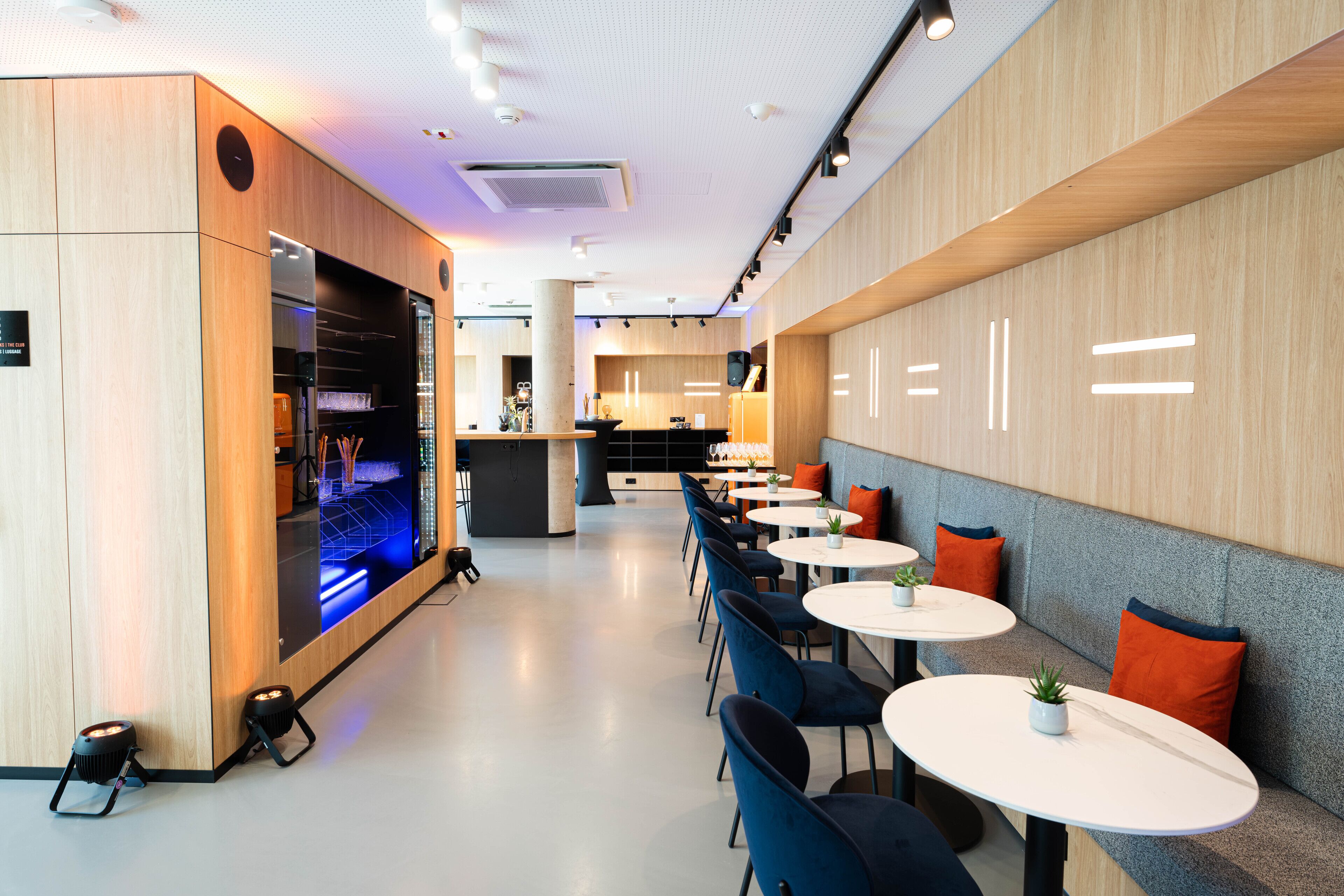 Un restaurant moderne avec des boiseries, des tables rondes et des chaises bleues.