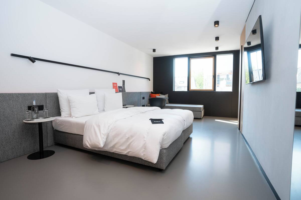 Ett modernt hotellrum med en stor säng, ett litet bord, en stol, ett fönster och en platt-TV.