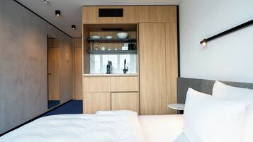 Una habitación de hotel moderna con una cama grande, una kitchenette integrada con cafetera y una pequeña mesa redonda.