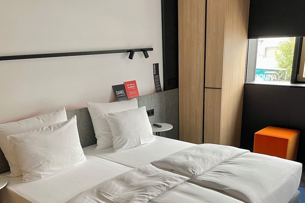 Ett modernt hotellrum med en stor säng, ett litet bord, en garderob och ett fönster med utsikt.