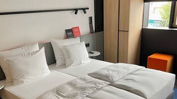 A modern hotel room with a large bed, a small table, a wardrobe, and a window with a view.