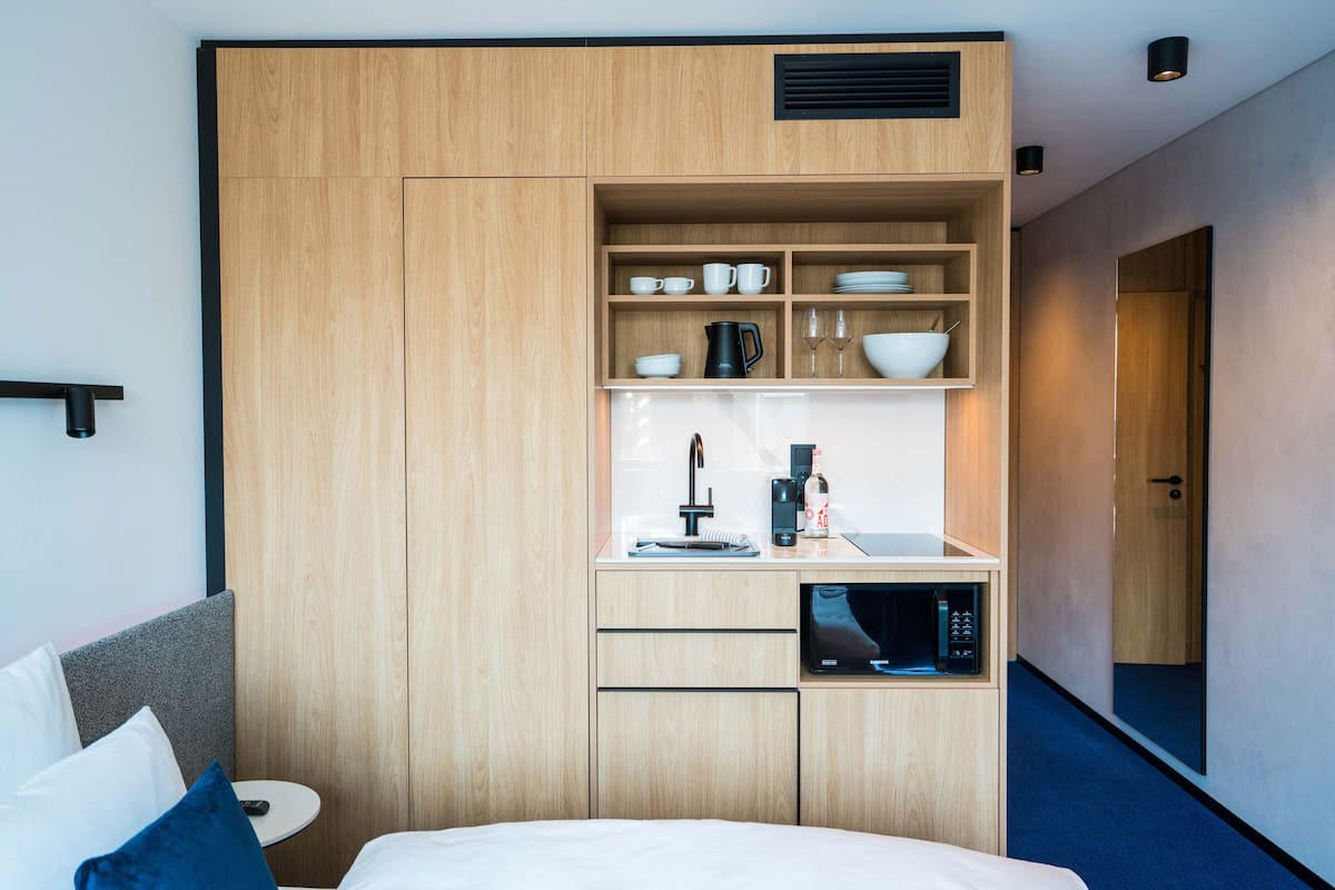 Ett kompakt hotellrum med en säng, ett litet pentry och en inbyggd mikrovågsugn.