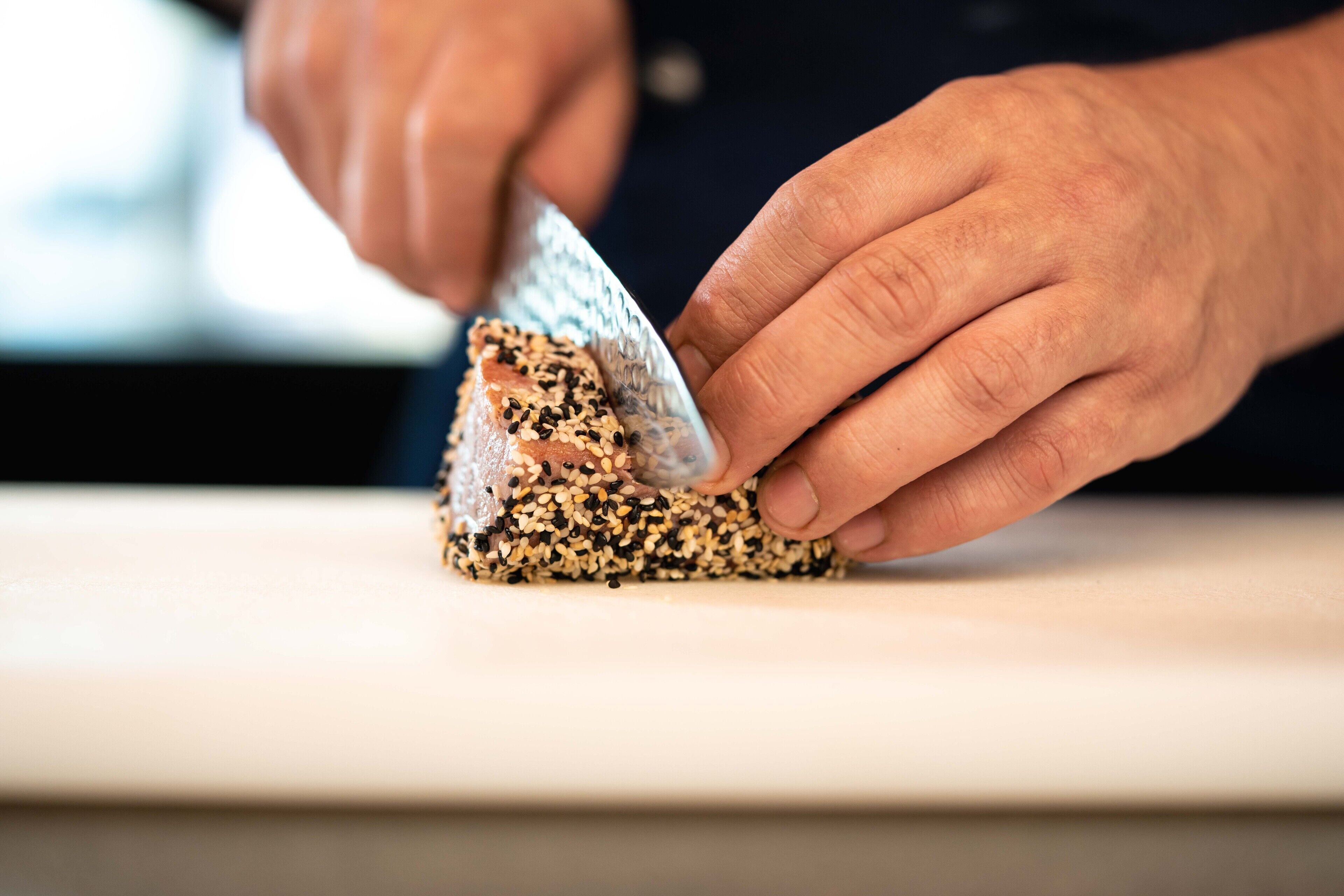 A person preparing food, specifically a sandwich with sesame seeds.