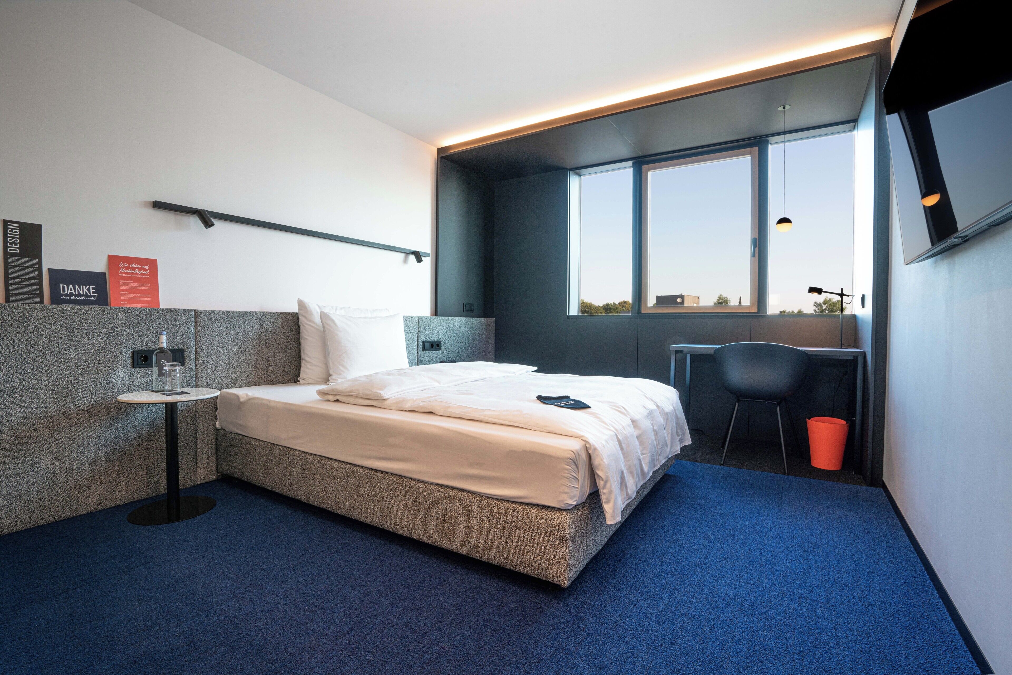 Habitación de hotel moderna con cama, una mesita, una silla y ventana con vistas.