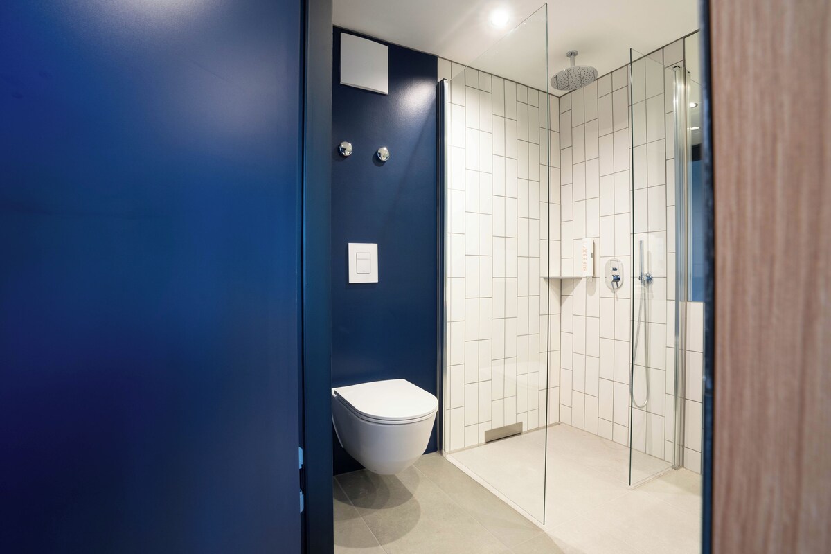A modern bathroom with a toilet, a shower with glass doors, and a blue accent wall.