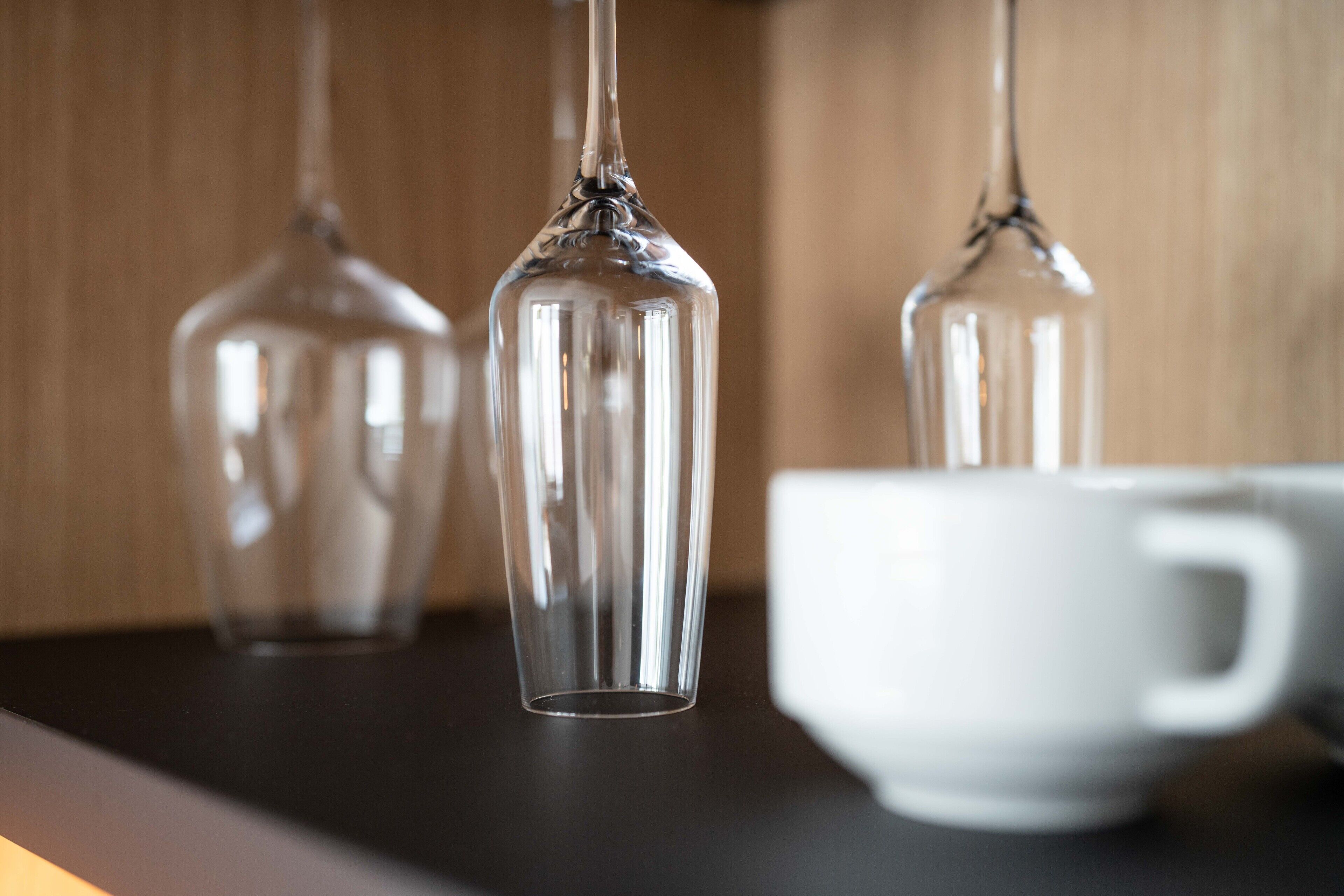 Three clear glass vases on a dark surface with a white cup in the background.