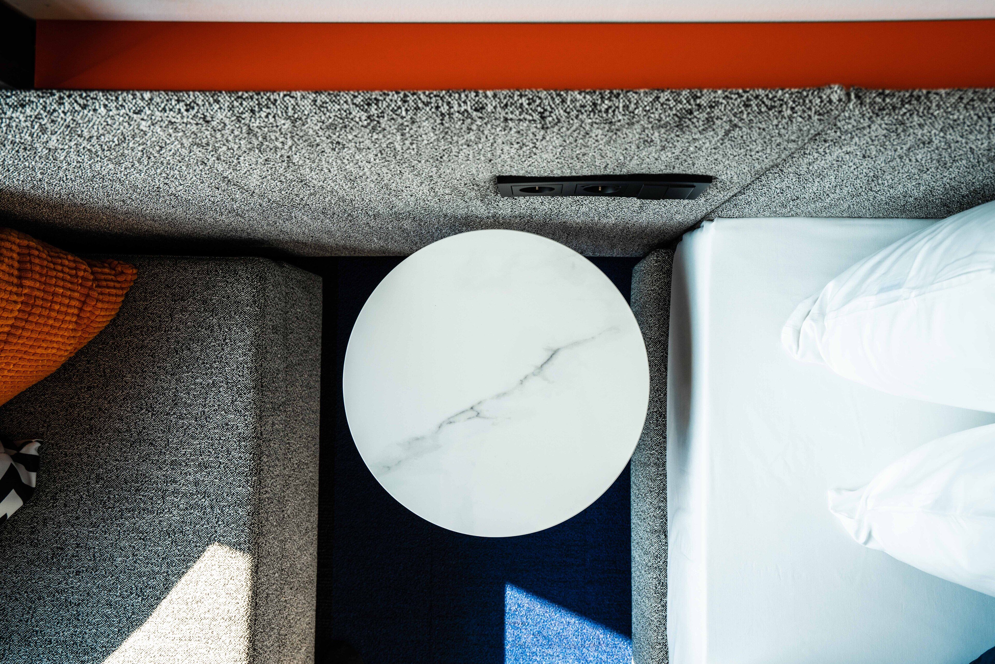 A modern room with a grey textured wall, a circular white marble table, and a bed with white linens.